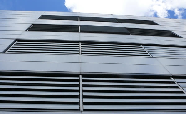 Povećani prikaz pročelja moderne zgrade s vodoravnim metalnim lamelama i panelima, snimljen prema djelomično oblačnom nebu.